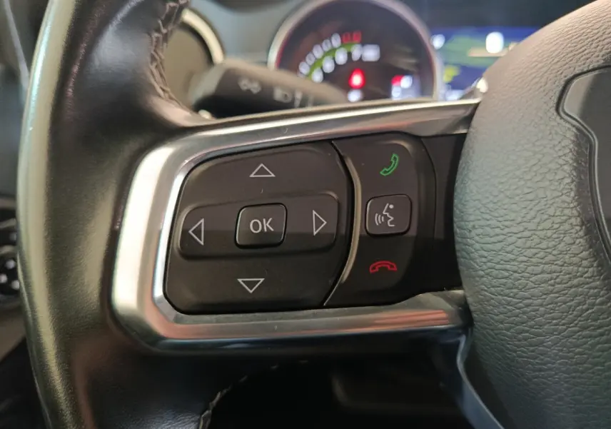 Gros plan sur les commandes gauche du volant cuir du Jeep Wrangler gris foncé, avec tableau de bord flou en arrière-plan.