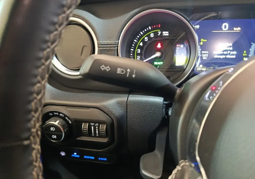 Gros plan sur le tableau de bord et volant cuir du Jeep Wrangler hybride gris foncé, avec affichage numérique et commandes lumineuses.