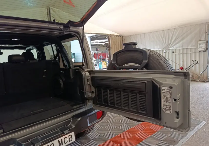 Vue arrière ouverte du Jeep Wrangler gris foncé, montrant le coffre vide et la roue de secours fixée sur la porte.