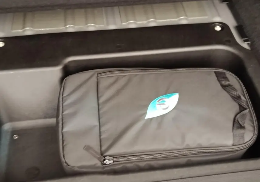 Rangement sous plancher avec sac de charge noir marqué d’un logo bleu dans le coffre d’un Jeep Wrangler gris foncé.