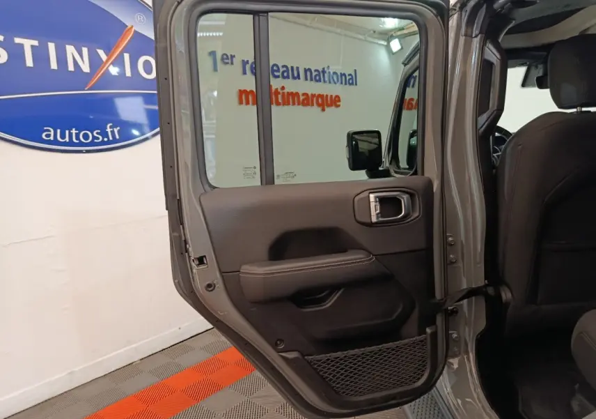 Vue intérieure côté gauche de la porte arrière ouverte d’un Jeep Wrangler gris foncé, avec garniture noire et filet de rangement.
