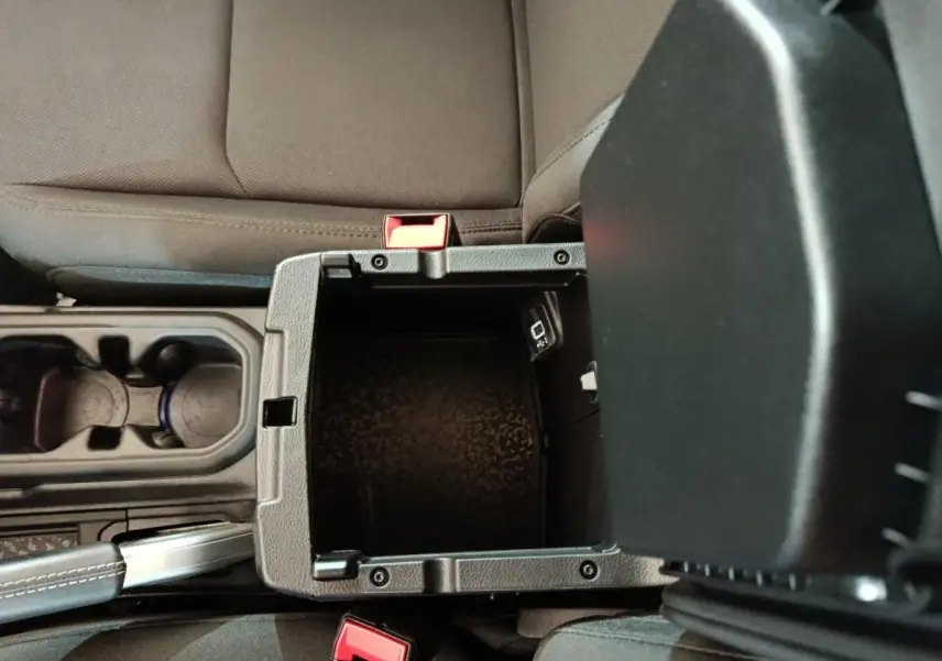 Vue plongeante sur la console centrale ouverte du Jeep Wrangler 2022, montrant un rangement noir entre les sièges gris foncé.