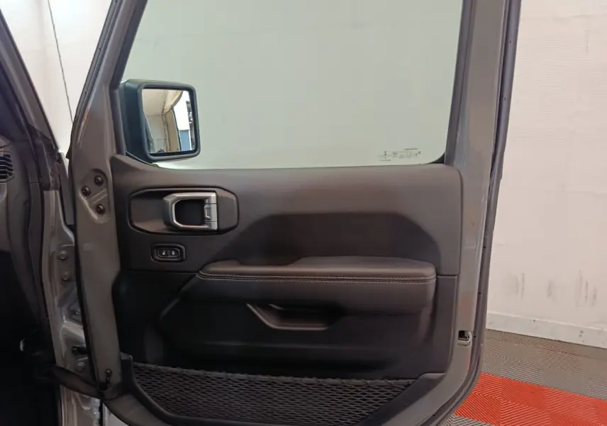Vue intérieure de la porte avant gauche gris foncé du Jeep Wrangler 2022 avec poignée et filet de rangement.