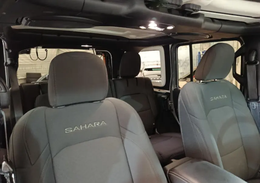 Vue intérieure avant de la Jeep Wrangler Sahara 2022, sièges gris foncé avec logo Sahara brodé, toit cabriolet ouvert.