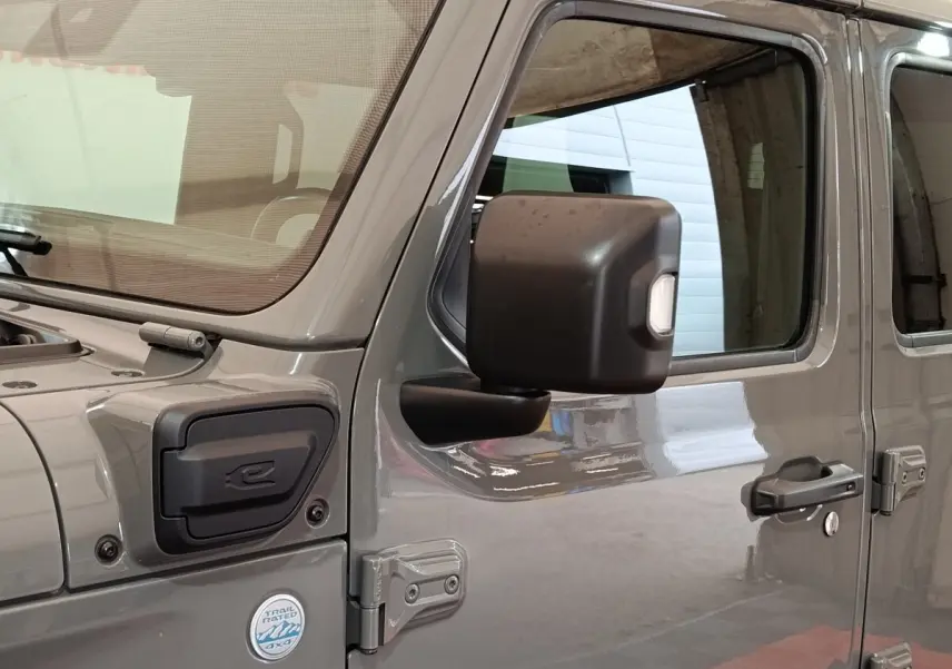 Vue latérale droite d’un Jeep Wrangler gris foncé hybride avec rétroviseur noir et badge Trail Rated 4x4.