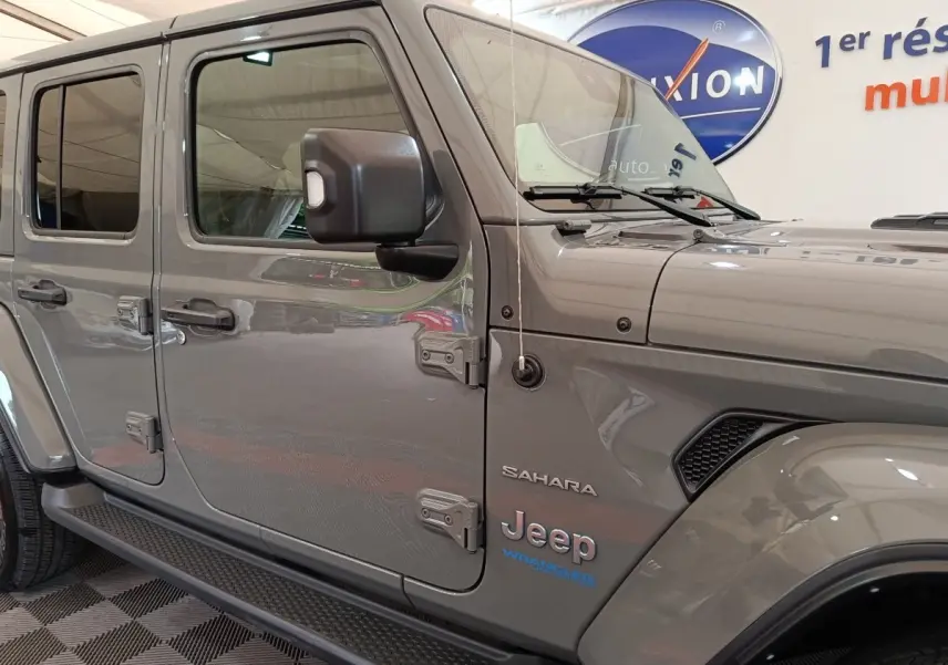 Vue latérale gauche d’un Jeep Wrangler Sahara gris foncé avec logo et détails de la version hybride rechargeable visibles.