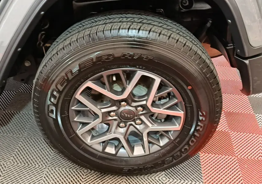Gros plan sur la roue avant droite du Jeep Wrangler gris foncé, mettant en valeur la jante aluminium et le pneu Bridgestone.