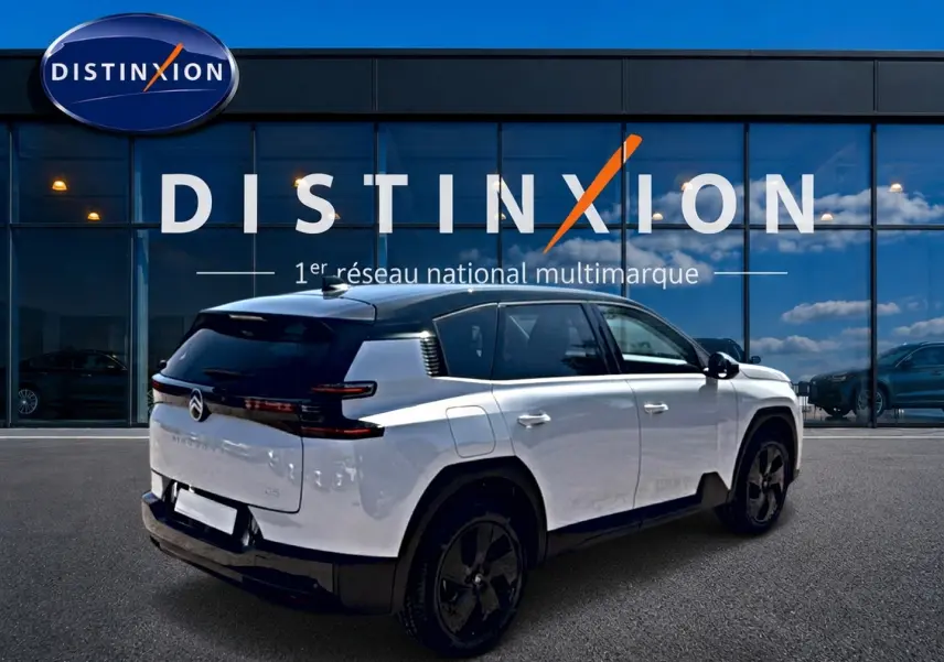 Vue 3/4 arrière droite d'un Citroën C5 Aircross blanc à toit noir avec jantes alliage noires devant un bâtiment Distinxion.