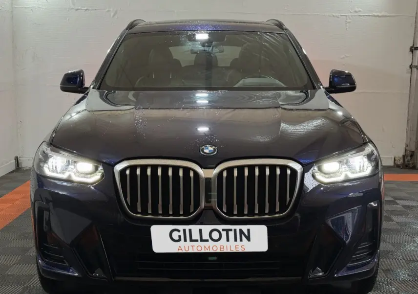 Vue frontale d’un BMW X3 xDrive30e bleu avec phares LED allumés et calandre imposante en intérieur showroom.