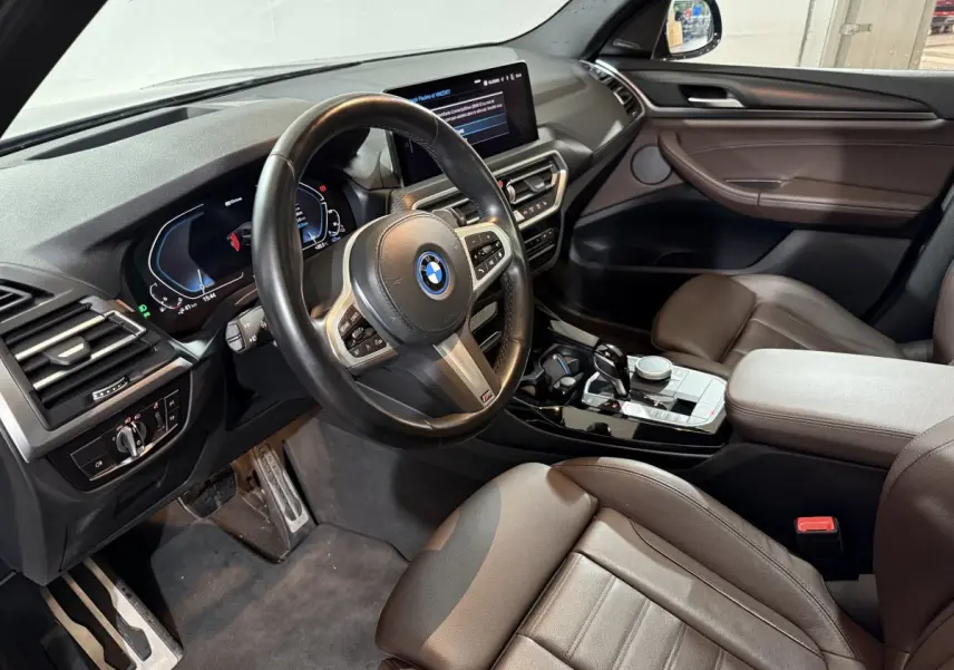 Vue intérieure côté conducteur du BMW X3 xDrive30e 2023 avec tableau de bord digital et sellerie cuir marron.