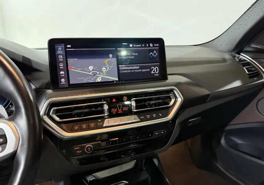 Vue intérieure du tableau de bord du BMW X3 xDrive30e 2023 avec écran tactile et commandes climatisation digitales.
