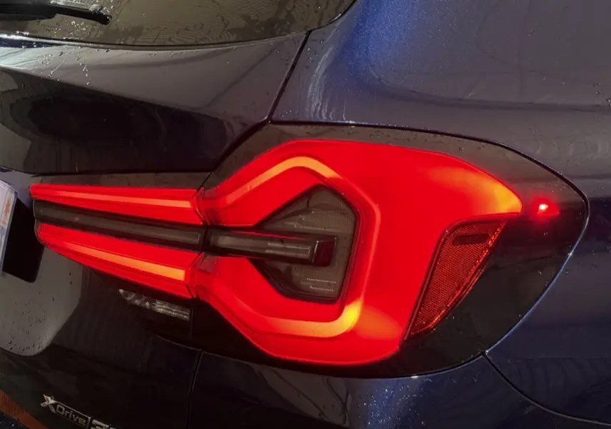 Feu arrière droit allumé sur BMW X3 xDrive30e bleu, avec logo xDrive visible sur la carrosserie.