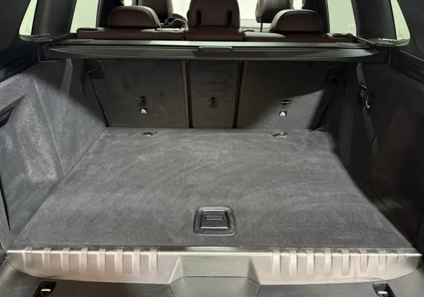 Vue intérieure du coffre spacieux et tapis noir du BMW X3 xDrive30e 2023, avec banquette arrière rabattue partiellement visible.