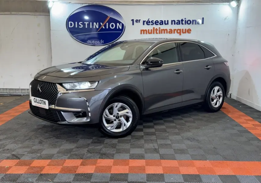 DS7 Crossback gris foncé en 3/4 avant droit, avec calandre distinctive et jantes alliage visibles en intérieur showroom.