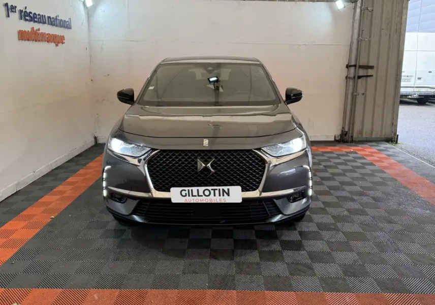 Vue frontale d'un DS7 Crossback gris foncé avec calandre distinctive et phares LED allumés dans un garage.