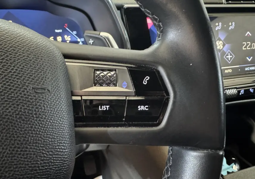 Gros plan sur le volant cuir noir du DS7 Crossback 2020 avec commandes audio et écran tactile de climatisation en arrière-plan.