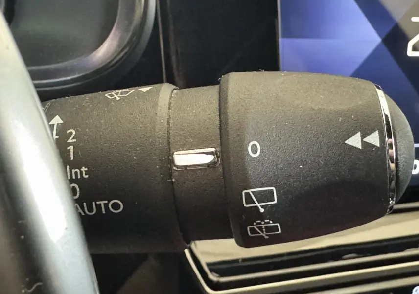 Gros plan sur la commande des essuie-glaces du DS7 Crossback gris foncé, avec tableau de bord numérique en arrière-plan.