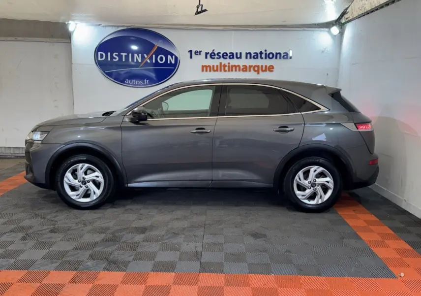 Vue latérale droite d'un DS7 Crossback gris foncé garé en intérieur avec vitres teintées et jantes argentées.