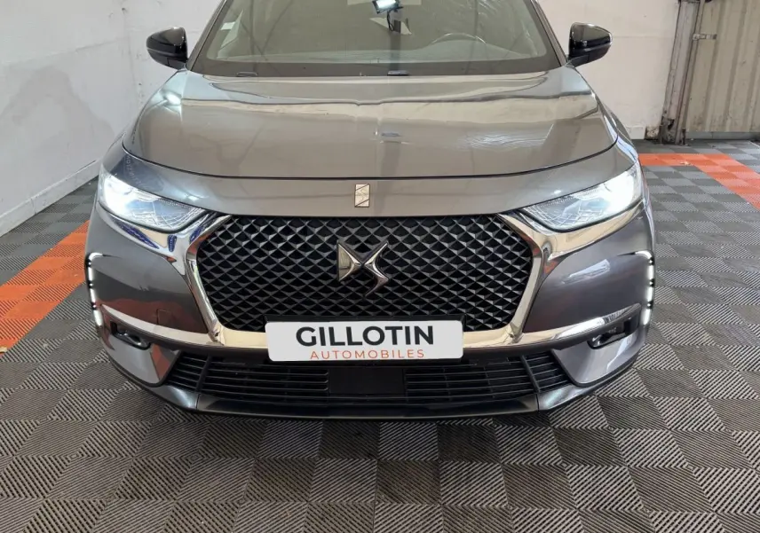 Vue avant d’un DS7 Crossback gris foncé avec calandre hexagonale et feux LED allumés dans un garage.