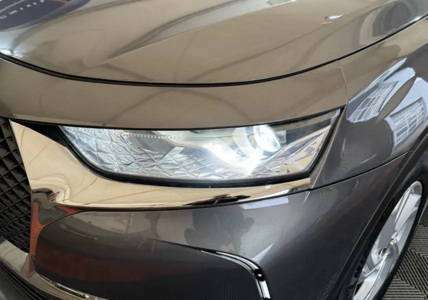 Gros plan sur le phare avant droit allumé d’un DS7 Crossback gris foncé, avec détails chromés autour de la calandre.