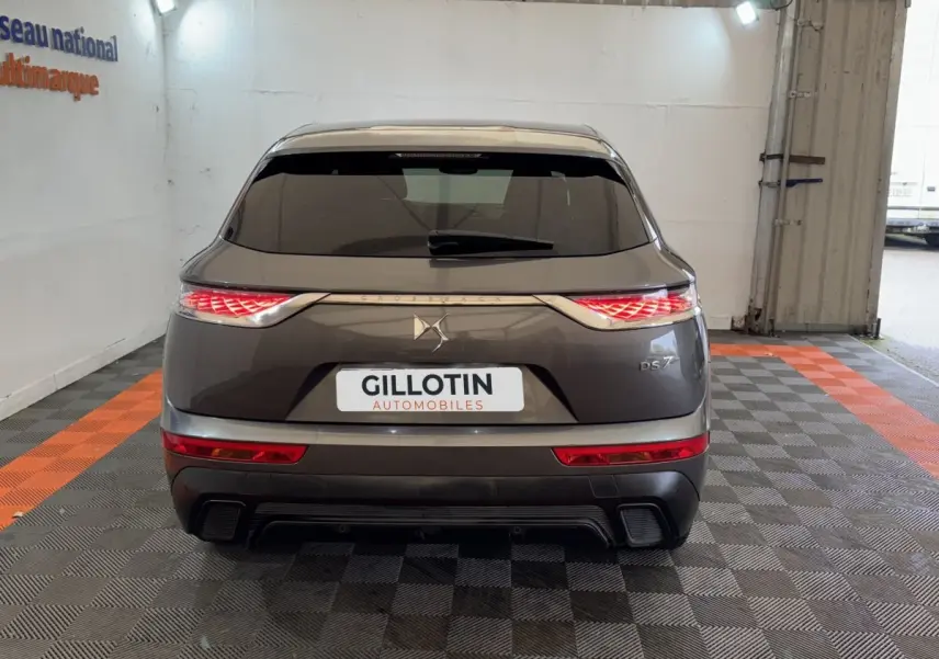 Vue arrière du DS7 Crossback gris foncé avec feux LED distinctifs et logo DS centré sur un fond clair intérieur.