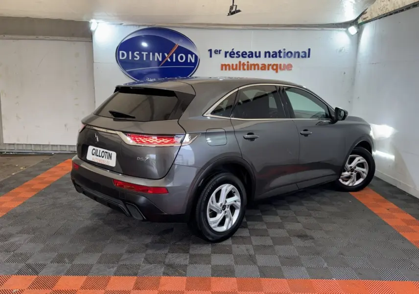 Vue 3/4 arrière droite d’un DS7 Crossback gris foncé stationné en intérieur avec feux arrière allumés.