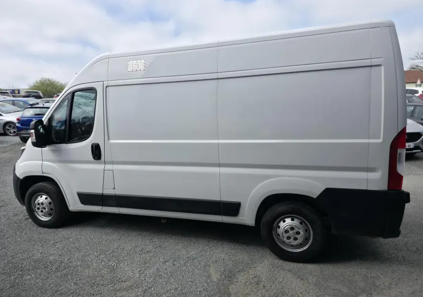 Vue de profil côté gauche d’un utilitaire Peugeot Boxer blanc avec porte latérale coulissante et baguettes de protection noires.