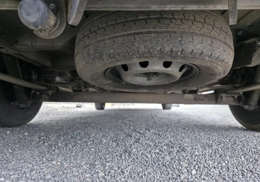 Vue en contre-plongée sous un Peugeot Boxer Fourgon blanc, montrant la roue de secours sous le châssis arrière.