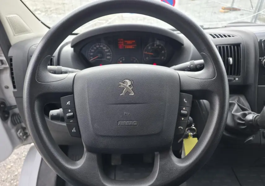 Vue rapprochée du volant noir avec logo Peugeot du Boxer Fourgon 2022, tableau de bord et levier de vitesses visibles.