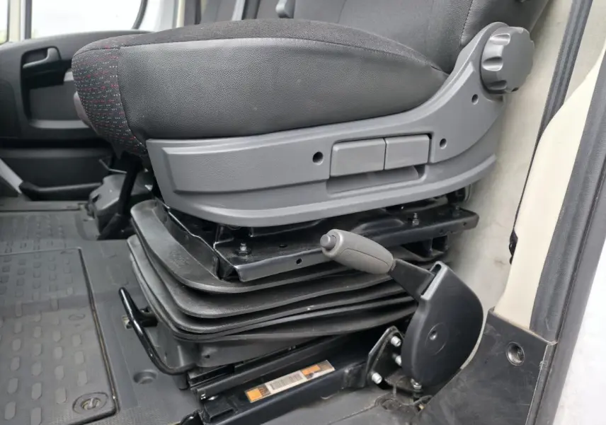 Gros plan sur le siège conducteur suspendu gris foncé du Peugeot Boxer Fourgon blanc, côté gauche intérieur cabine.