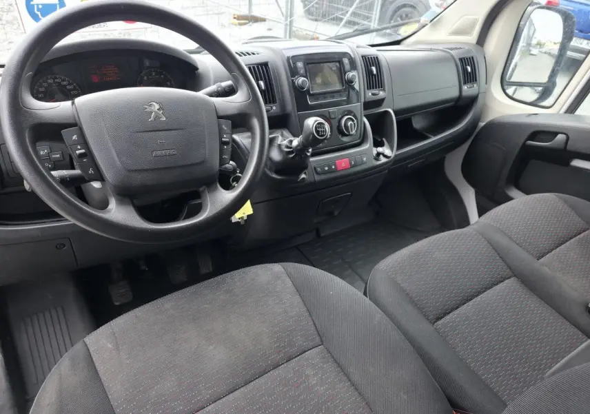 Vue intérieure côté conducteur du Peugeot Boxer Fourgon 2022, volant noir, sièges tissu gris foncé avec motifs rouges.
