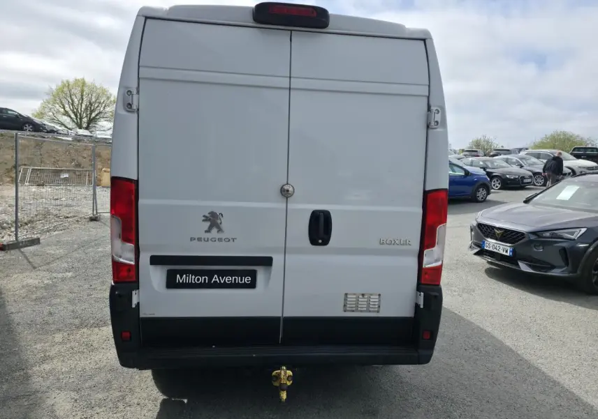 Vue arrière d’un Peugeot Boxer blanc avec crochet d’attelage et portes battantes fermées sur parking.