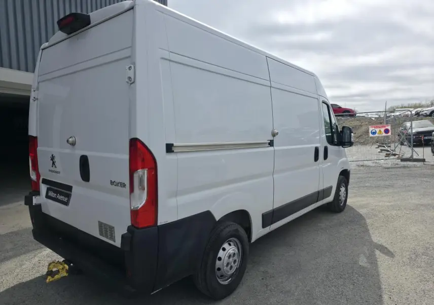 Vue 3/4 arrière droite du Peugeot Boxer Fourgon blanc avec crochet d'attelage et baguettes latérales noires.