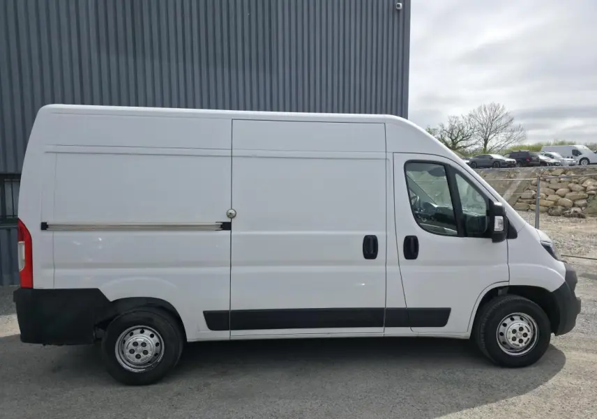 Peugeot Boxer Fourgon blanc vu de profil côté droit, avec porte latérale coulissante et enjoliveurs noirs.