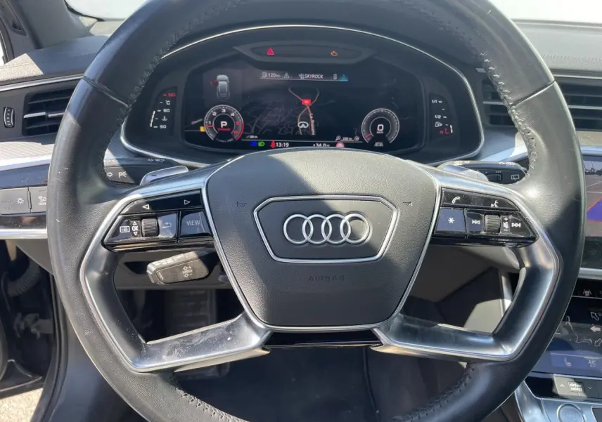 Vue rapprochée du volant en cuir multifonction d’une Audi A6 2019, avec tableau de bord numérique et commandes intégrées.