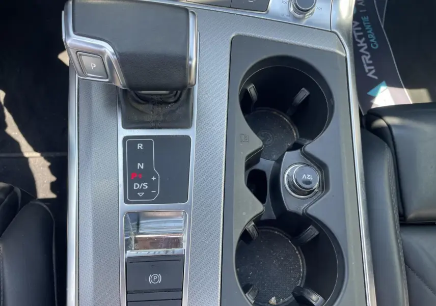 Gros plan sur la console centrale de l’Audi A6 noire, avec levier de vitesse automatique et porte-gobelets.