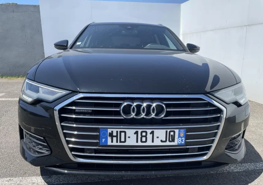Vue avant d'une Audi A6 noire métal 2019 avec calandre chromée et phares Full LED allumés.