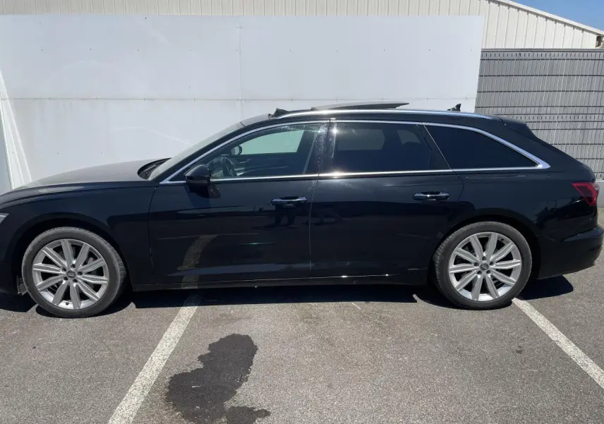 Profil latéral droit d'une Audi A6 Avant noire métallisée avec jantes aluminium 10 branches et vitres surteintées.