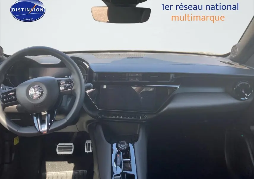 Vue intérieure frontale de l'Alfa Romeo Junior 1.2 hybride 2026, tableau de bord noir avec écran tactile et volant multifonction.
