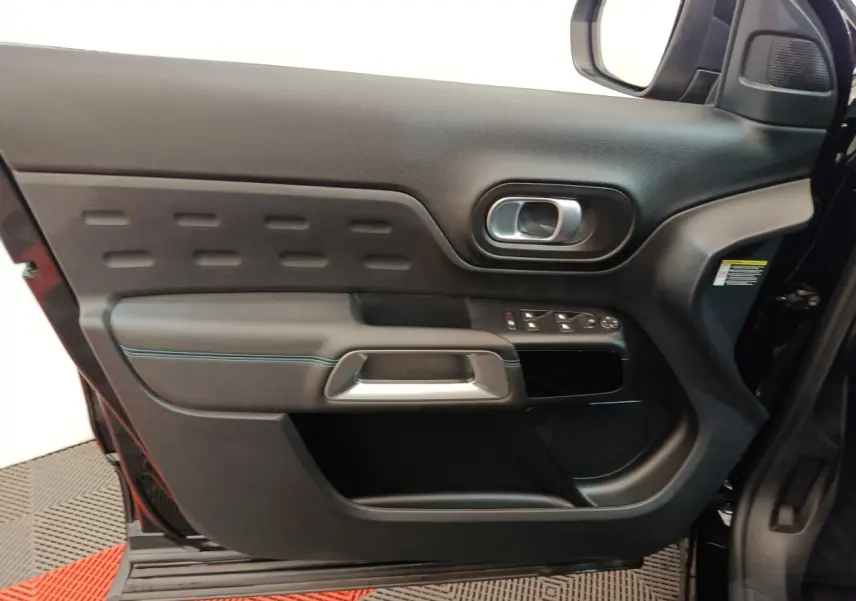 Vue intérieure côté gauche de la porte noire du Citroën C5 Aircross 2024 avec commandes de vitres et poignée argentée.