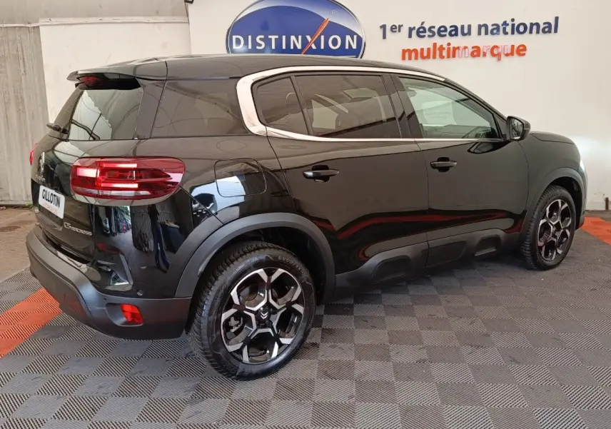 Vue 3/4 arrière droite d'un Citroën C5 Aircross noir 2024 avec jantes distinctives et barres de toit chromées.