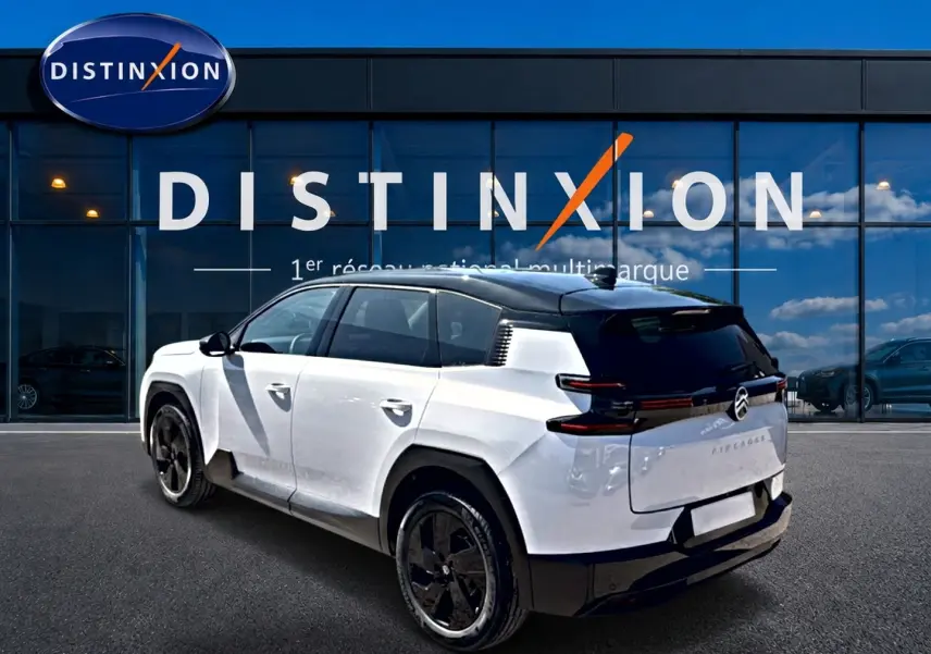 Vue 3/4 arrière droite du Citroën C5 Aircross hybride blanc avec toit noir et jantes alliage noires devant un showroom Distinxion.