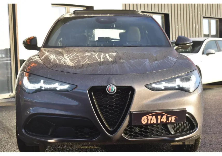 Vue avant d'un Alfa Romeo Stelvio 2024 gris Vesuvio métallisé avec feux LED allumés et calandre caractéristique en V.