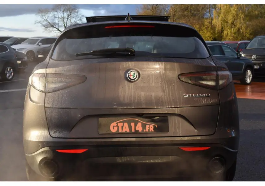 Vue arrière d'un Alfa Romeo Stelvio gris Vesuvio avec toit ouvrant panoramique et logo visible sous la lumière du jour.