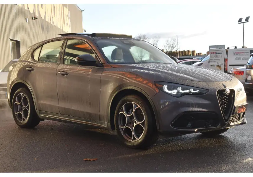 Alfa Romeo Stelvio gris Vesuvio en 3/4 avant droit, avec jantes 19'' Competizione et toit panoramique ouvert.