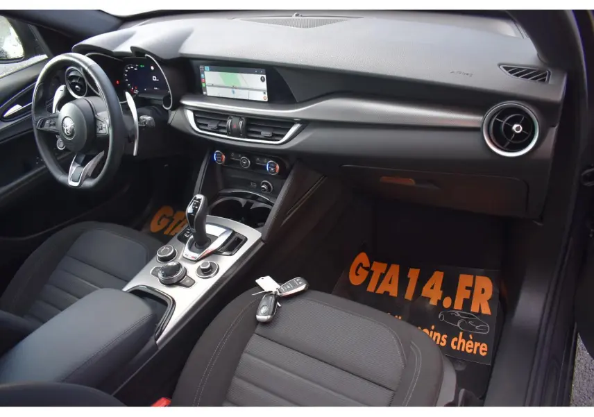 Intérieur de l'Alfa Romeo Stelvio 2024 vu côté conducteur, tableau de bord moderne avec écran tactile et volant sport.