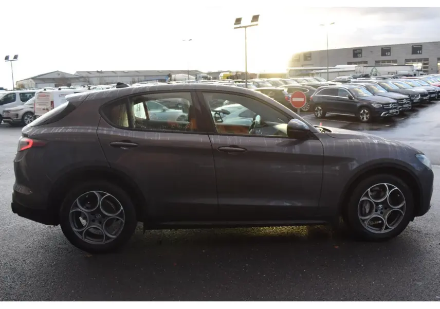 Profil côté gauche de l'Alfa Romeo Stelvio 2024 gris Vesuvio avec jantes 19'' Competizione et toit panoramique visible.