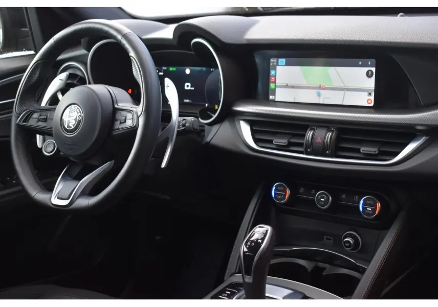 Intérieur de l'Alfa Romeo Stelvio 2024 vu côté conducteur, tableau de bord noir avec écran tactile et volant sport.