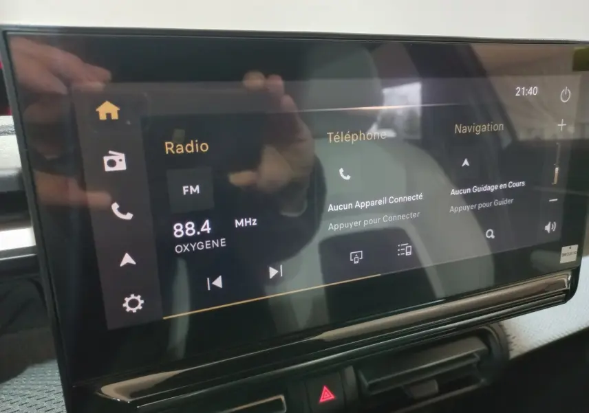 Écran tactile central de la Citroën C3 hybride 2025 affichant radio, téléphone et navigation, avec reflet de mains.