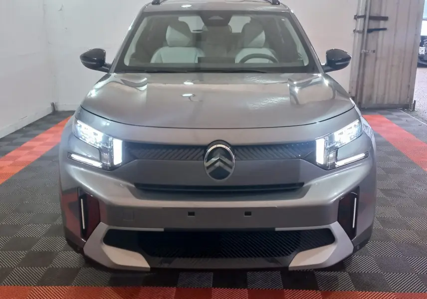 Vue frontale d'une Citroën C3 hybride gris foncé avec phares LED allumés dans un garage.